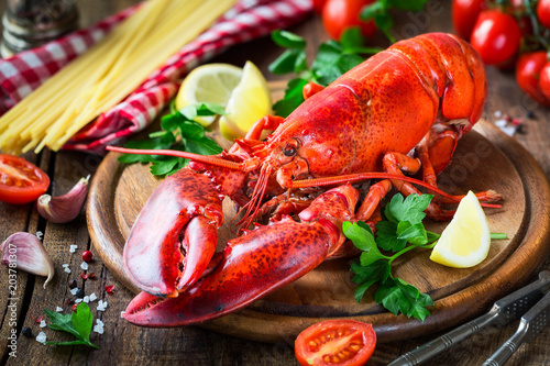 Steamed red lobster on a wooden cutting board with parsley, lemon wedges and spaghetti at the background. Spaghetti all'astice or Lobster spaghetti recipe