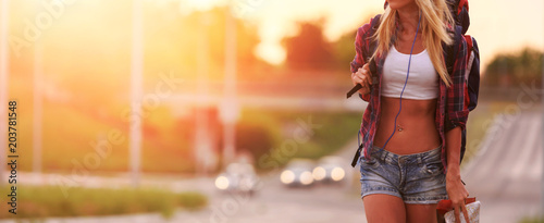 Beautiful young woman traveler with backpack walking along highway in sunset