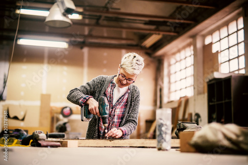 Happy short hair female working with the electric drill in a big garage.