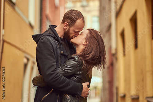 Bearded man and brunette girl kissing, on the background of the old European street.