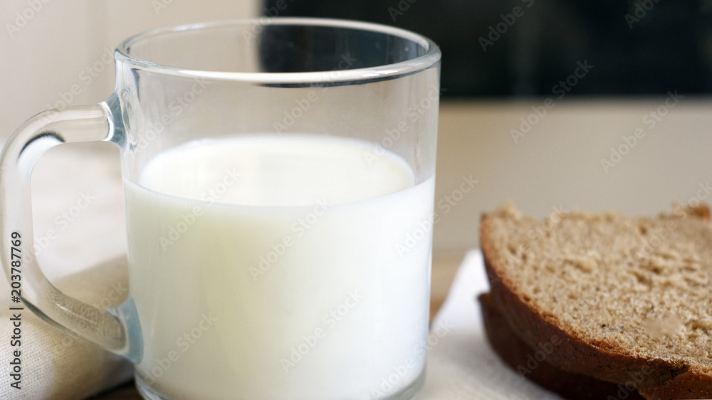 A glass of milk next to a slice of rye bread on the table A glass of milk next to a slice of rye bread on the table