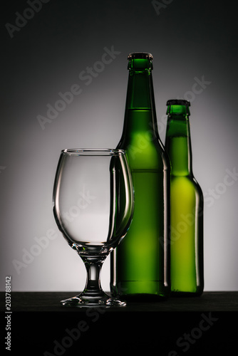 close up view of bottles of beer and empty glass on grey background