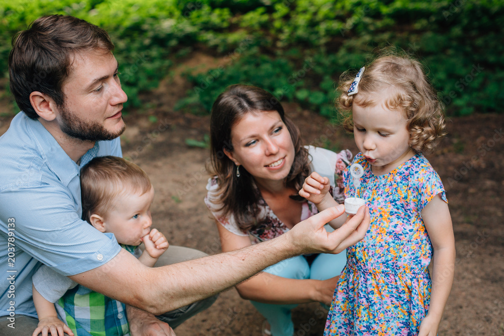 Fototapeta premium Happy family having fun in the park.Cute Little girl trying to inflate the soap