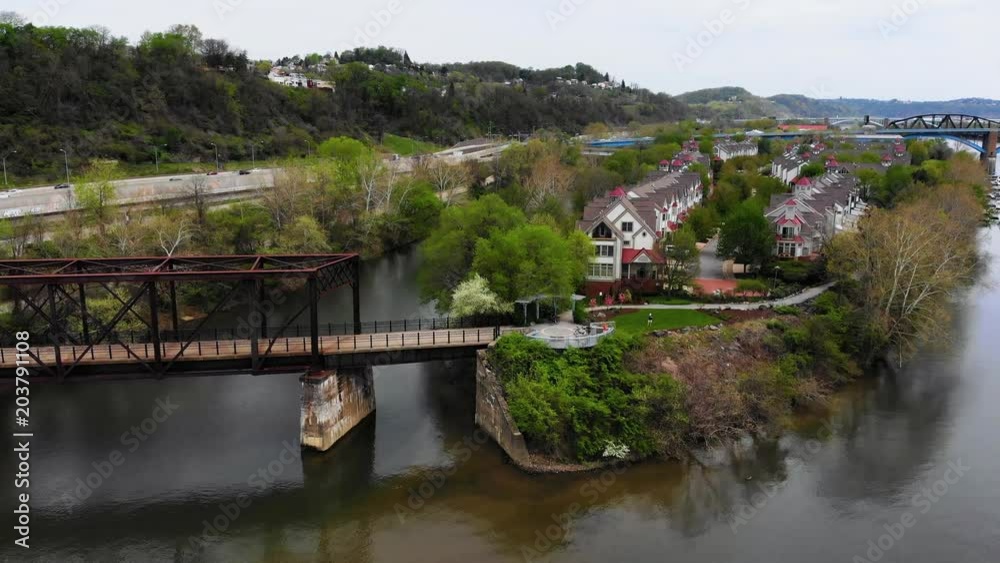 A daytime forward aerial establishing shot of Harrs Island in Pittsburgh as a bicyclist rides across the pedestrian bridge. A daytime forward aerial establishing shot of Harrs Island in Pittsburgh as a bicyclist rides across the pedestrian bridge.