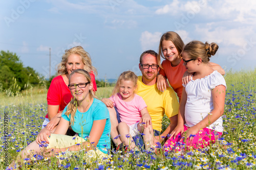 Family sitting on meadow in flowers, mom, dad and the kids