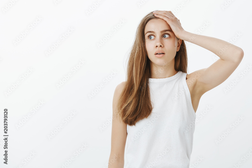 Worried forgetful attractive woman in casual clothes, looking left with opened mouth and holding palm on forehead, being shocked while remembering important meeting, standing over gray wall Worried forgetful attractive woman in casual clothes, looking left with opened mouth and holding palm on forehead, being shocked while remembering important meeting, standing over gray wall