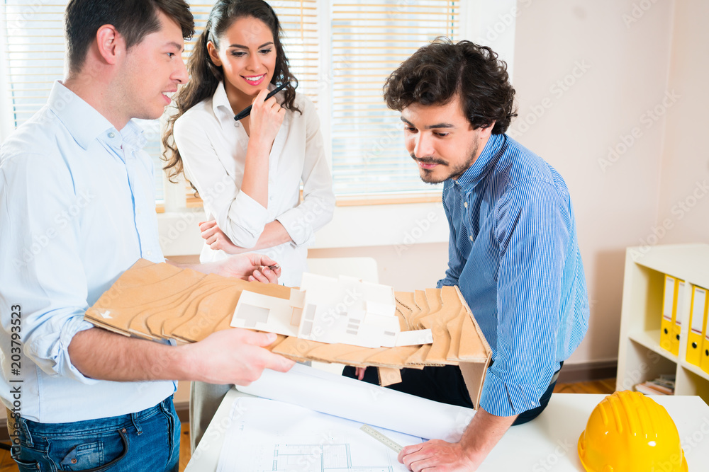 Construction engineers and architects discuss building project with model in office Construction engineers and architects discuss building project with model in office