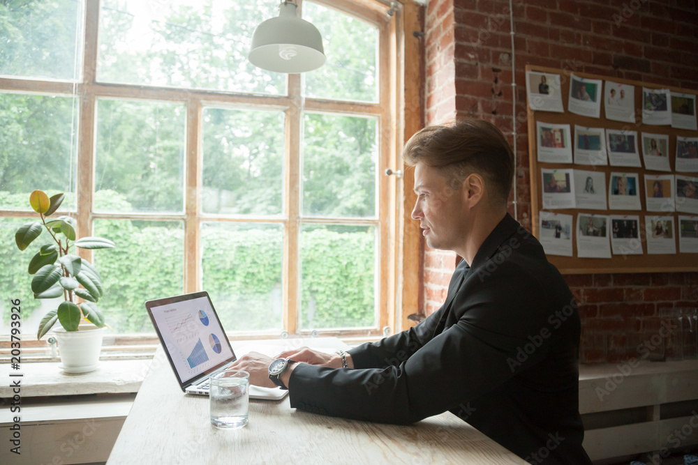 Successful male businessman working on laptop analyzing company financial reports with charts and diagrams in modern loft office. CEO analyzing profitability statistics and sales operations online Successful male businessman working on laptop analyzing company financial reports with charts and diagrams in modern loft office. CEO analyzing profitability statistics and sales operations online