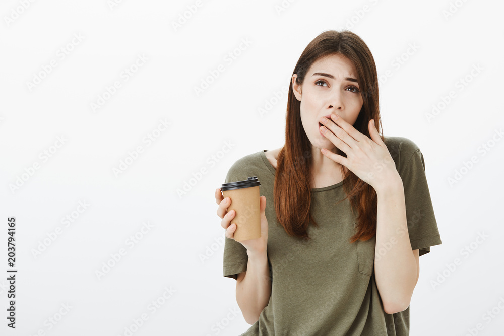 Indoor shot of tired and bored cute girlfriend in dark-green t-shirt, yawning, covering opened mouth with palm, drinking coffee not to fall asleep during daytime, overworking or hearing boring talks Indoor shot of tired and bored cute girlfriend in dark-green t-shirt, yawning, covering opened mouth with palm, drinking coffee not to fall asleep during daytime, overworking or hearing boring talks