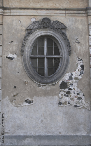Round window of the church morgue with skull and wings on the top. Vertical shot.
