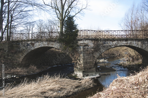 The old stone bridge with two arcs in gloomy and historical environment.