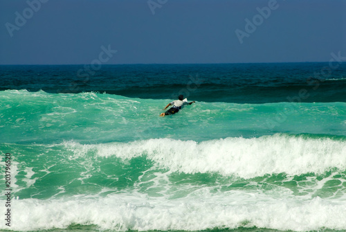 Surfer at the top of turquoise wave swimming towards deep dark sea