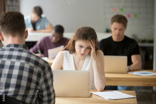 Disappointed female trader sad about bad news on stock exchange market browsing online on laptop in coworking space. Unhappy student thinking about problem solution seeking answers on internet.