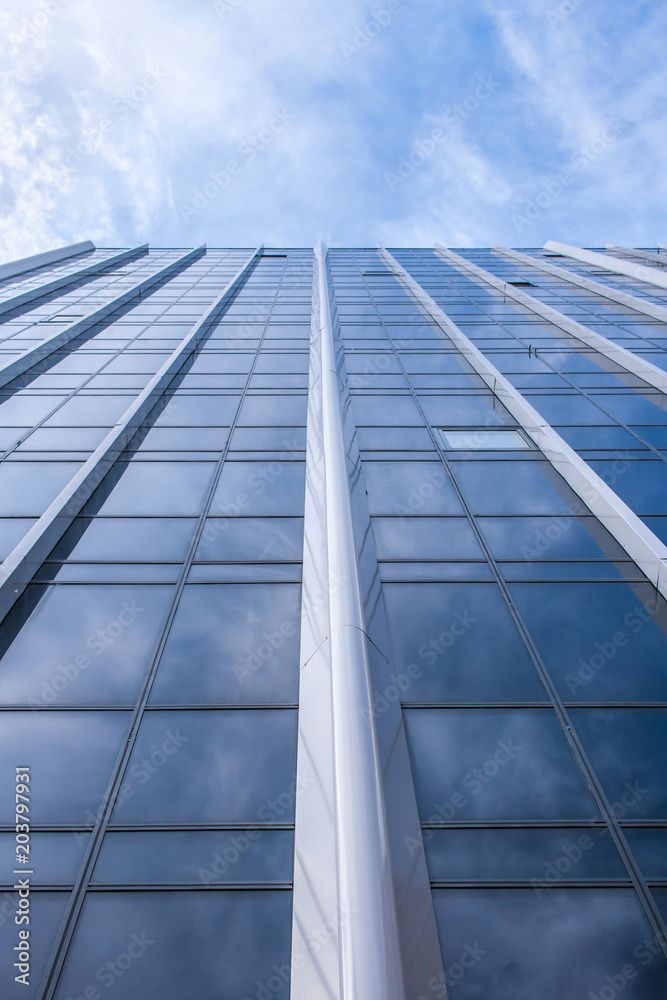 Bottom view of facade of modern glass building and cloudy blue sky up it. Perspective view. Bottom view of facade of modern glass building and cloudy blue sky up it. Perspective view.
