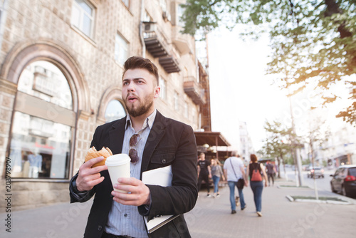 A busy man eats and drinks coffee while walking for work. Business man has breakfast with fast food. A businessman goes to work on the street and eats a sandwich photo