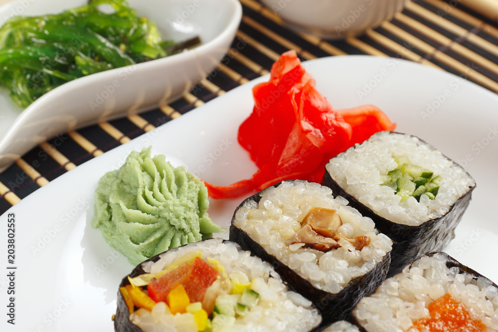 Sushi with ginger and wasabi and hiyashi wakame salad on a black bamboo mat close up.
