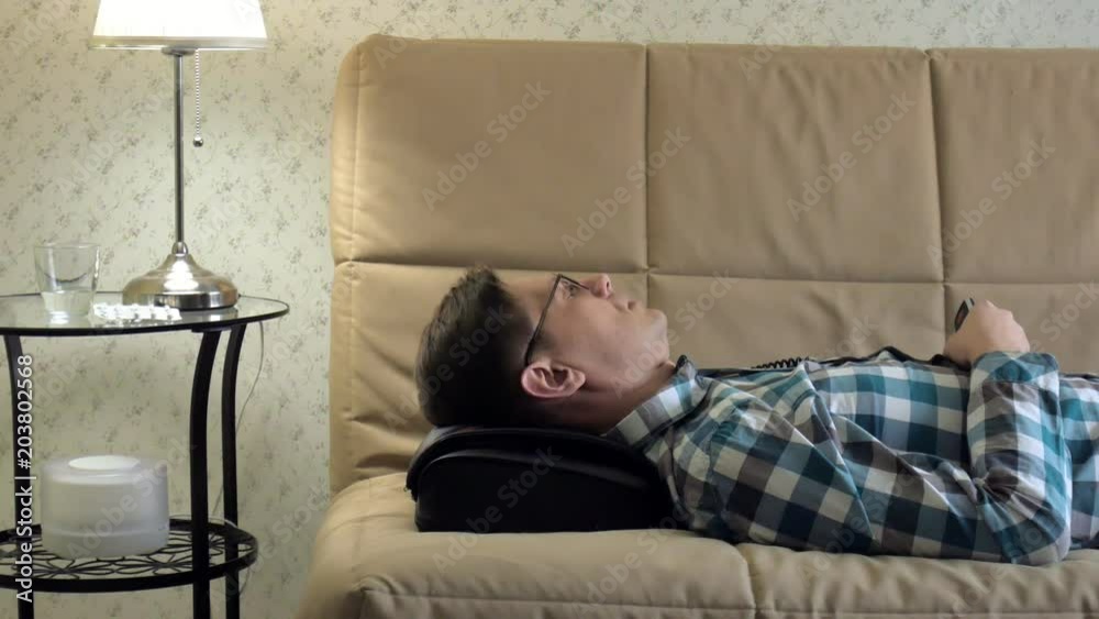 man lies on the couch at home, under the head of a massager, relaxed state man lies on the couch at home, under the head of a massager, relaxed state