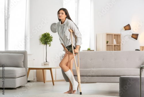 Obraz na plátne Young woman with crutch and broken leg in cast at home