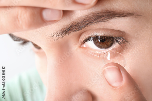 Young woman putting contact lens in her eye, closeup