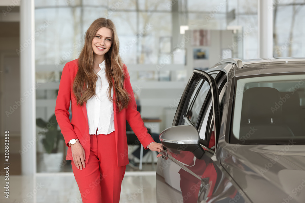 Young saleswoman near automobile in car dealership Young saleswoman near automobile in car dealership