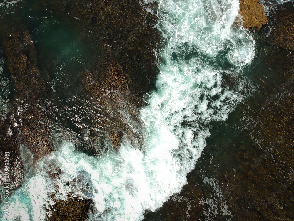 Aerial view of sea waves crash on the rocks in the coastline