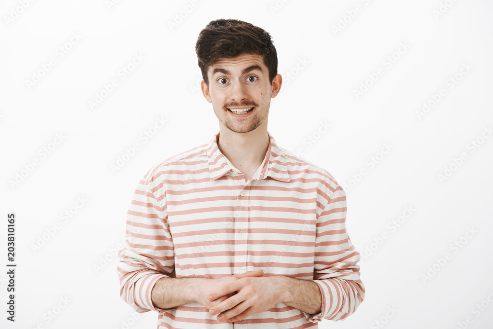 How may I help you. Portrait of friendly good-looking european shop assistant in striped shirt, holding hands together and offering help, talking casually and polite with customer over gray wall How may I help you. Portrait of friendly good-looking european shop assistant in striped shirt, holding hands together and offering help, talking casually and polite with customer over gray wall