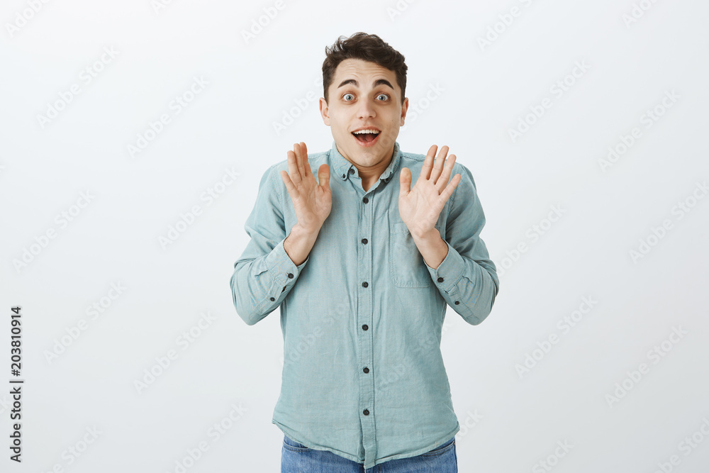 Indoor shot of excited happy male model in casual shirt, raising palms and gasping with broad smile, feeling thrilled and surprised, seeing awesome and amazing gift over gray background Indoor shot of excited happy male model in casual shirt, raising palms and gasping with broad smile, feeling thrilled and surprised, seeing awesome and amazing gift over gray background