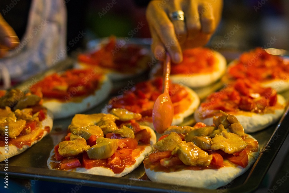 Bruschetta pizzas with diced roma tomatoes and shop assistant adding chicken pieces on top at night market in Koh Phangan island, Thailand