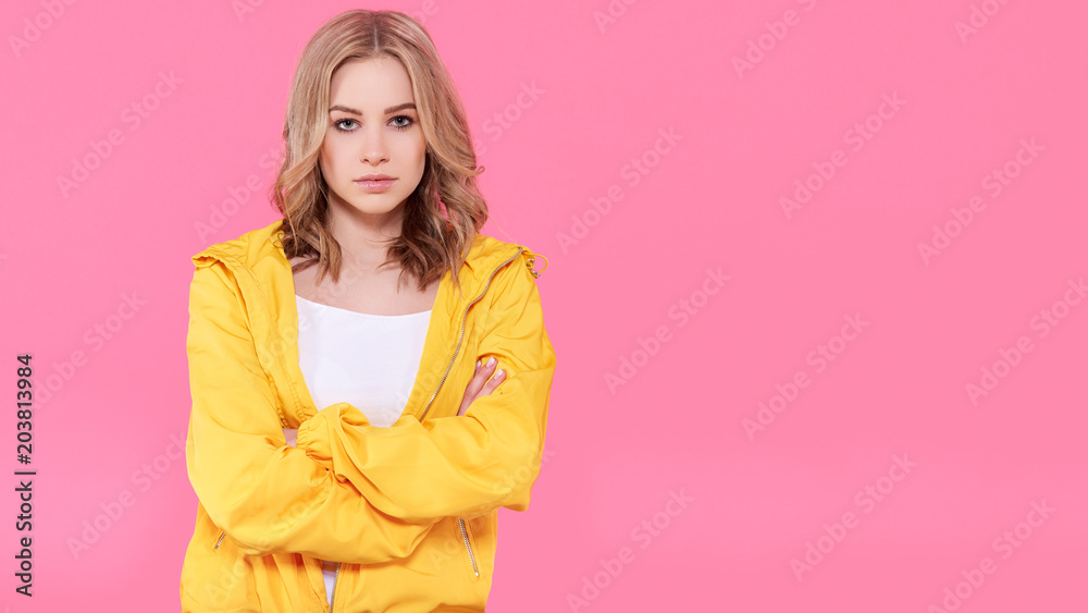 Beautiful trendy girl in bright yellow jacket and crossed arms. Attractive young woman portrait over pastel pink background. Confidence concept. Beautiful trendy girl in bright yellow jacket and crossed arms. Attractive young woman portrait over pastel pink background. Confidence concept.