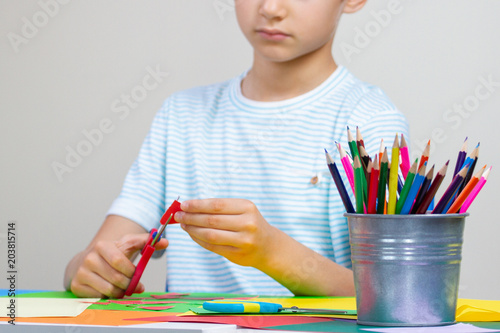Child hands cutting colored paper with scissors at the table