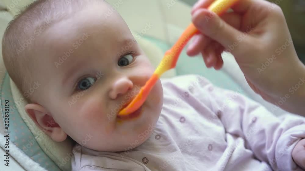 Mother feeding baby with orange spoon, close up shot Mother feeding baby with orange spoon, close up shot