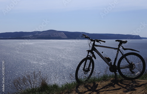 Silhouette of a sport bike against the background of a big river. There are mountains in the distance. Blue sky .