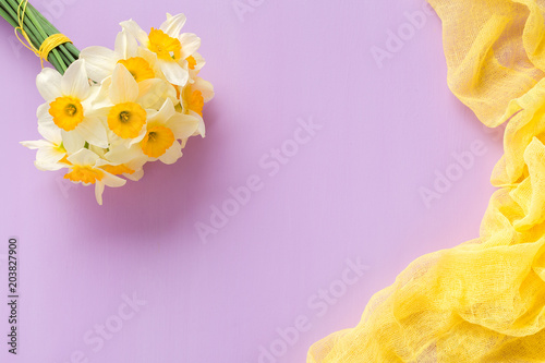 Fototapeta Naklejka Na Ścianę i Meble -  Daffodil bouquet with yellow textile decoration on violet pastel background with copy space.