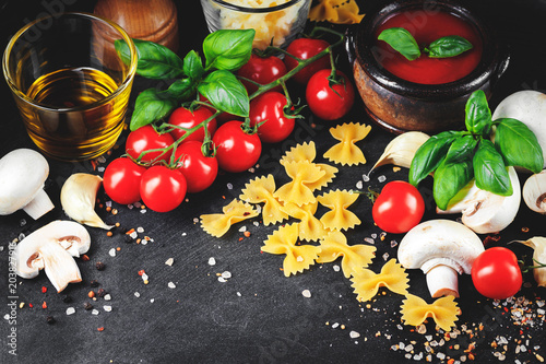 Italian pasta ingredients. Cherry-tomatoes, farfalle pasta, garlic, mushroom, basil, olive oil, mozzarella and spices on dark grunge backdrop