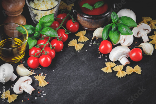 Italian pasta ingredients. Cherry-tomatoes, farfalle pasta, garlic, mushroom, basil, olive oil, mozzarella and spices on dark grunge backdrop with place for copy space
