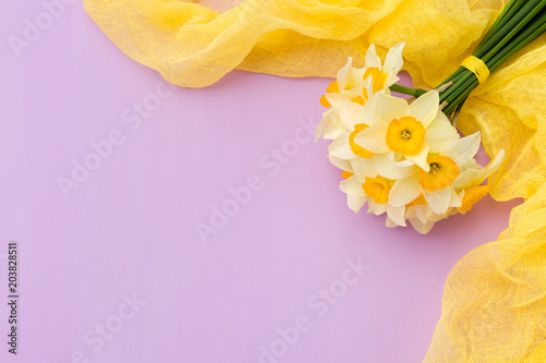 Fototapeta Naklejka Na Ścianę i Meble -  Daffodil bouquet with yellow textile decoration on violet pastel background with copy space.