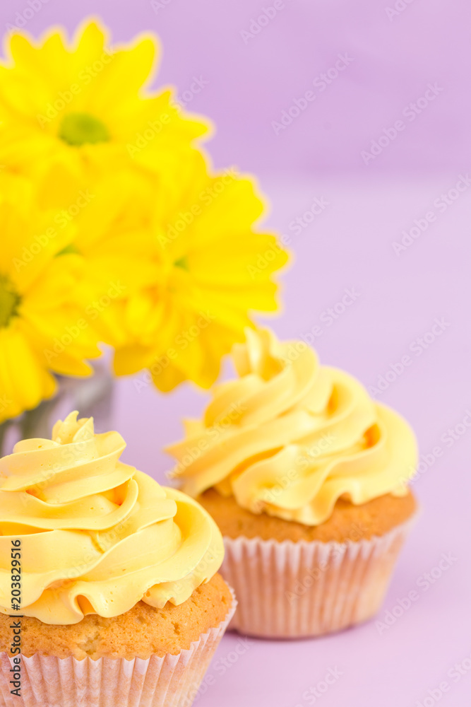Cupcakes decorated with yellow cream and chrysanthemums on violet pastel background. Cupcakes decorated with yellow cream and chrysanthemums on violet pastel background.