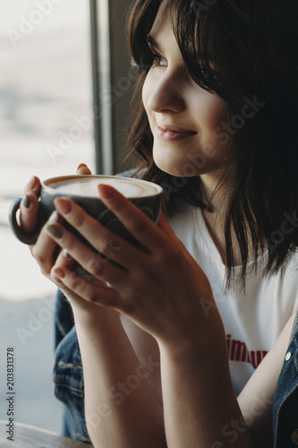 Close up portrait of a charming brunette drinking coffee and looking away through the window .