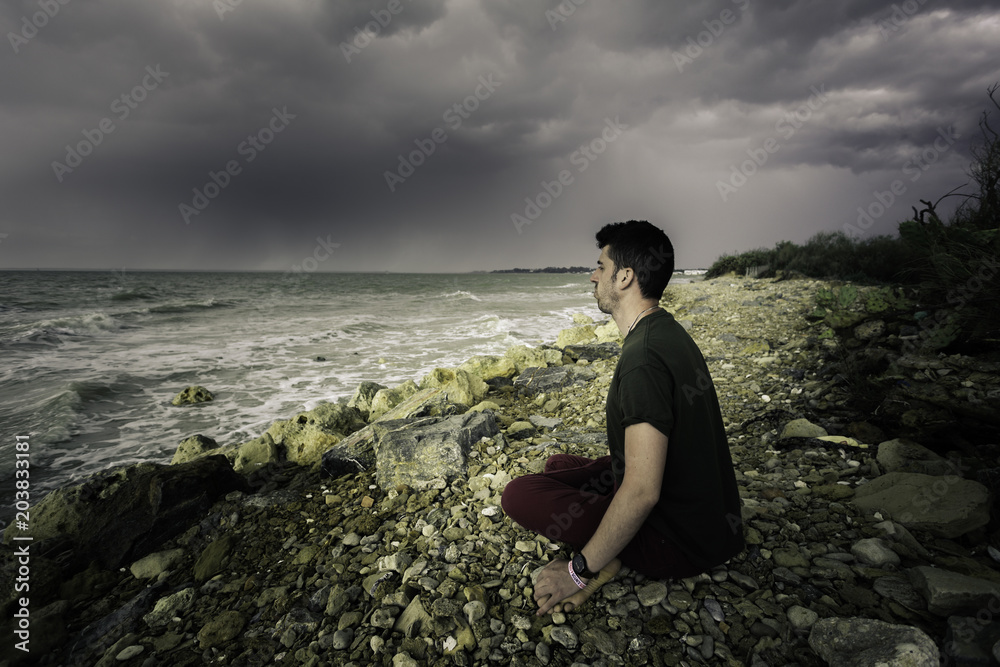 Hombre joven sentado a orillas del mar meditando con el yoga