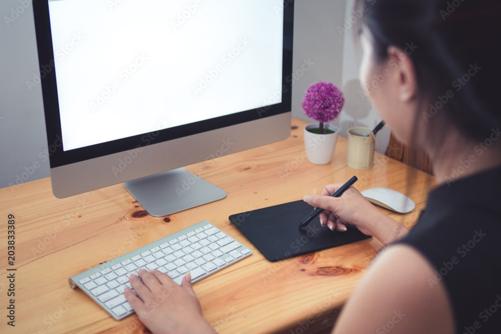 Beautiful Young Asian Woman hipster graphic designer using digital graphic tablet while working at modern office, professional retoucher sitting at modern workspace with wooden table.Designer concepts Beautiful Young Asian Woman hipster graphic designer using digital graphic tablet while working at modern office, professional retoucher sitting at modern workspace with wooden table.Designer concepts
