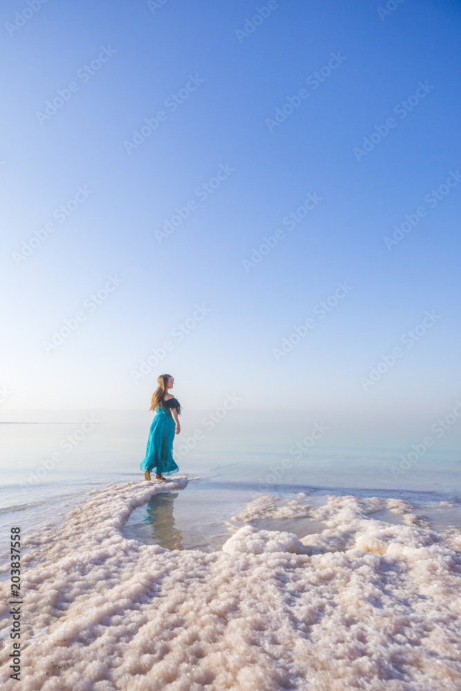 Blonde young woman in a blue dress on the shore of the dead sea. Jordan