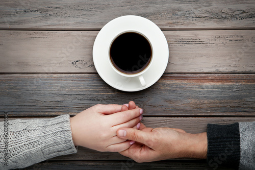 Female and male hand holding each other with cup of coffee