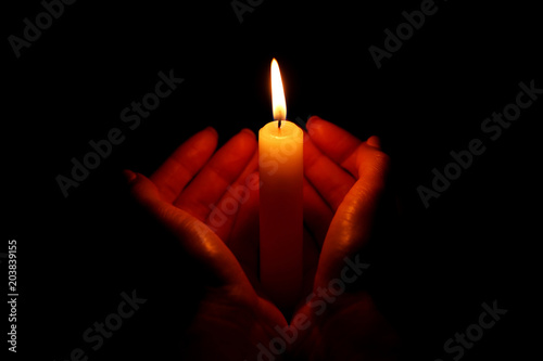 Female hands holding burning candle on black background