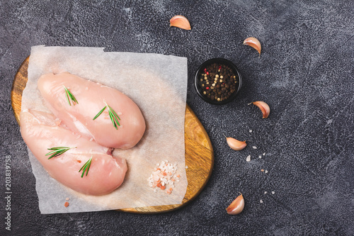 Raw chicken breast with rosemary, garlic and spices on wooden cutting board. Dark stone background. Ready for cooking.  Top flat view