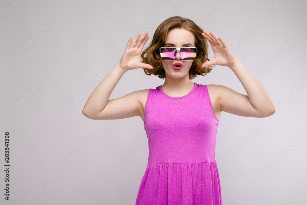 Charming young girl in pink dress on gray background. Cheerful girl in square glasses. Charming young girl in pink dress on gray background. Cheerful girl in square glasses.
