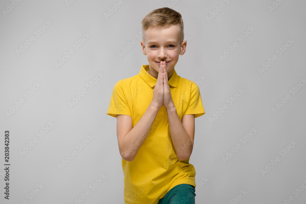 Portrait of cute little blonde caucasian boy in yellow t-shirt hoping on gray background Portrait of cute little blonde caucasian boy in yellow t-shirt hoping on gray background
