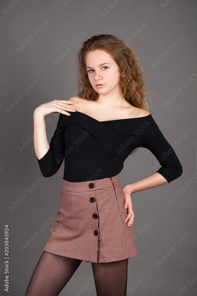 Portrait curly blonde in a black blouse and short skirt, on gray studio wall Portrait curly blonde in a black blouse and short skirt, on gray studio wall