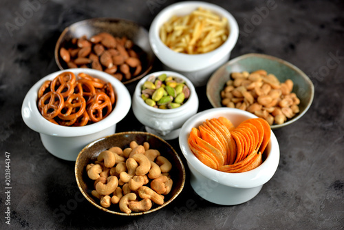 Different kinds of snacks - chips, salted peanuts, cashews, almonds and pistachios, pretzels with salt, potatoes, salted straw.
