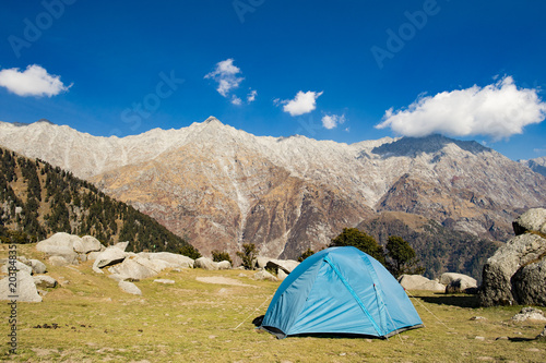 A single blue tent seen against Dhaulahaar peaks of Himalayas in Triund. Sunny day whit some clouds. Dharamshala, Himachal Pradesh. India