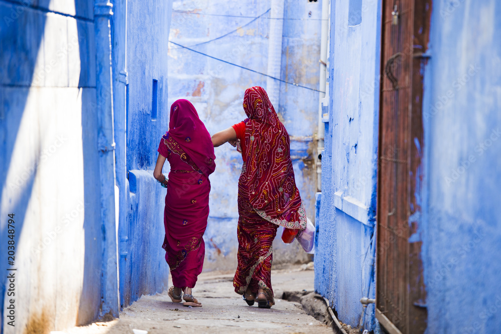 Two women dressed in the traditional Indian Saree are walking through the narrow streets of the blue city of Jodhpur, Rajasthan, India.